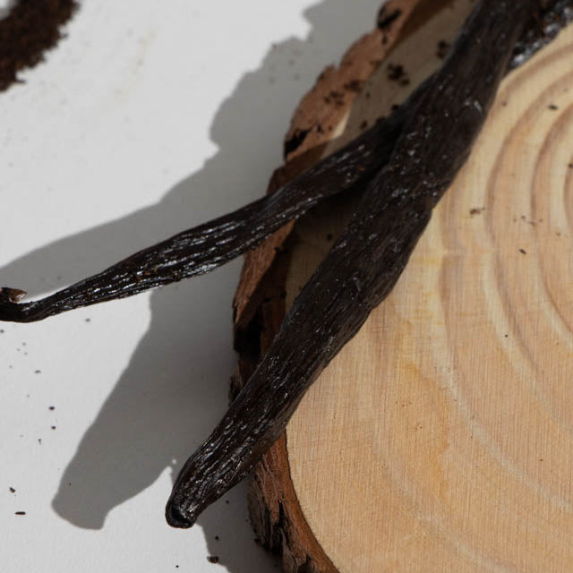Vanilla beans on a wooden surface with a white background